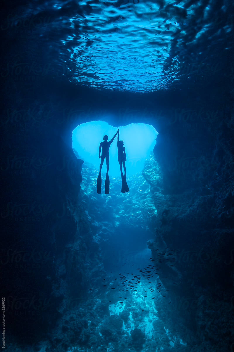Couple free divers holding hands in the heart shape cavern with back light