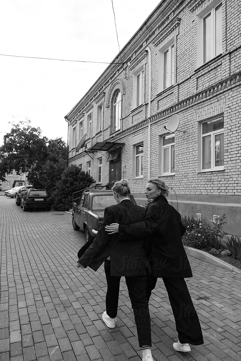 black and white photo of two sisters walking side by side along the street and hugging each other