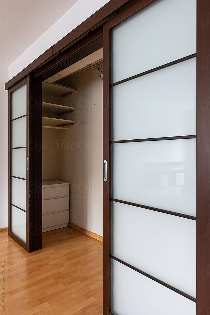 Empty closet with brown glass sliding door open inside small apartment