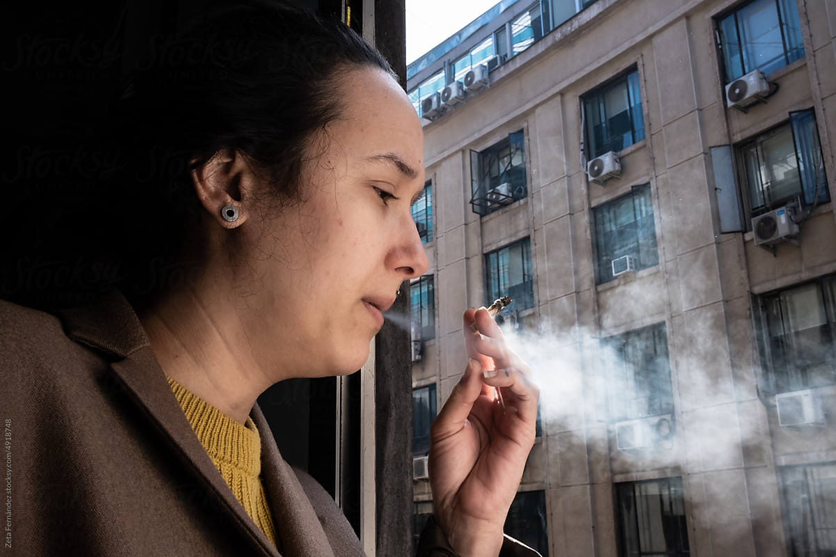 woman smokes tobacco at the window and throws the smoke outside