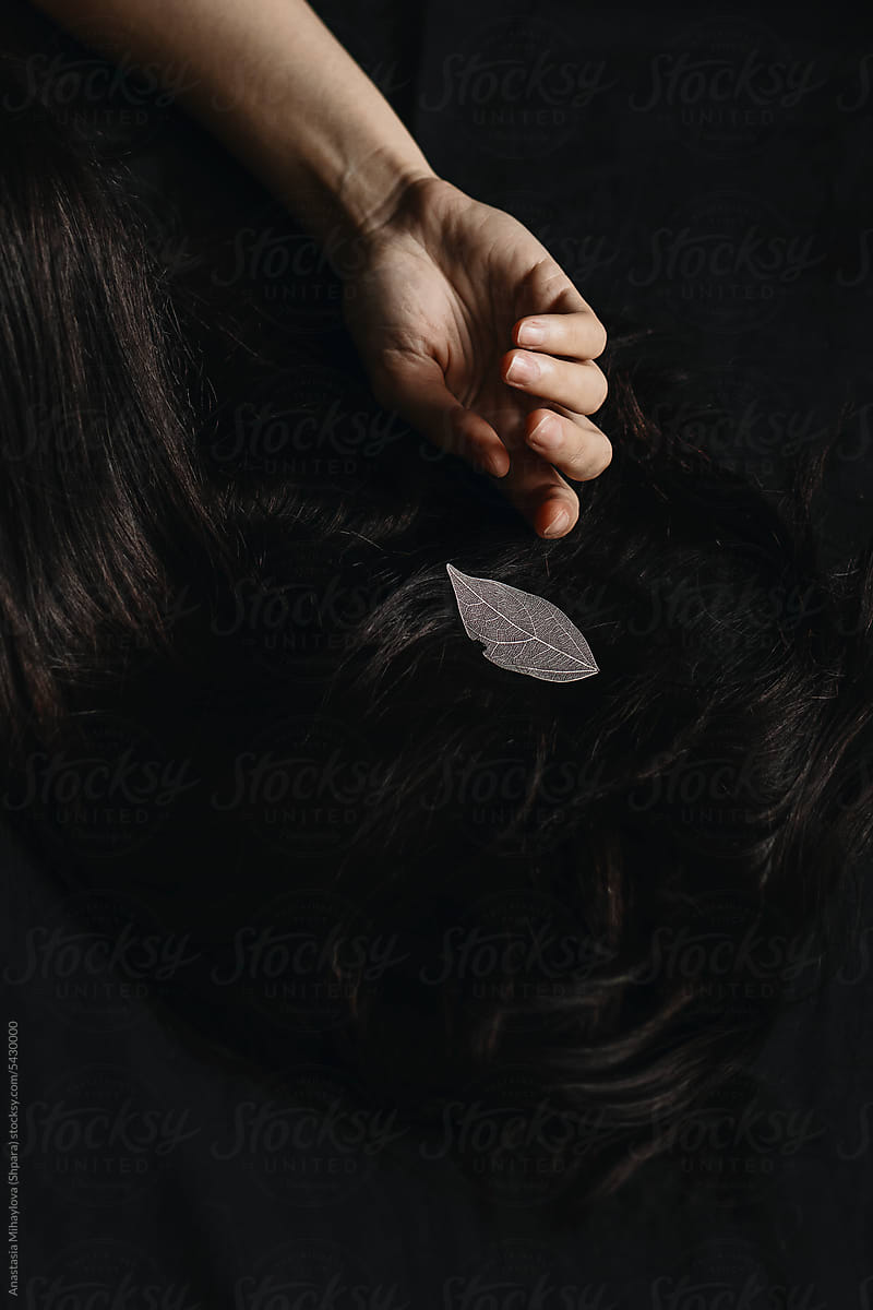 CloseUp long woman's dark hair with white leaf on the black background