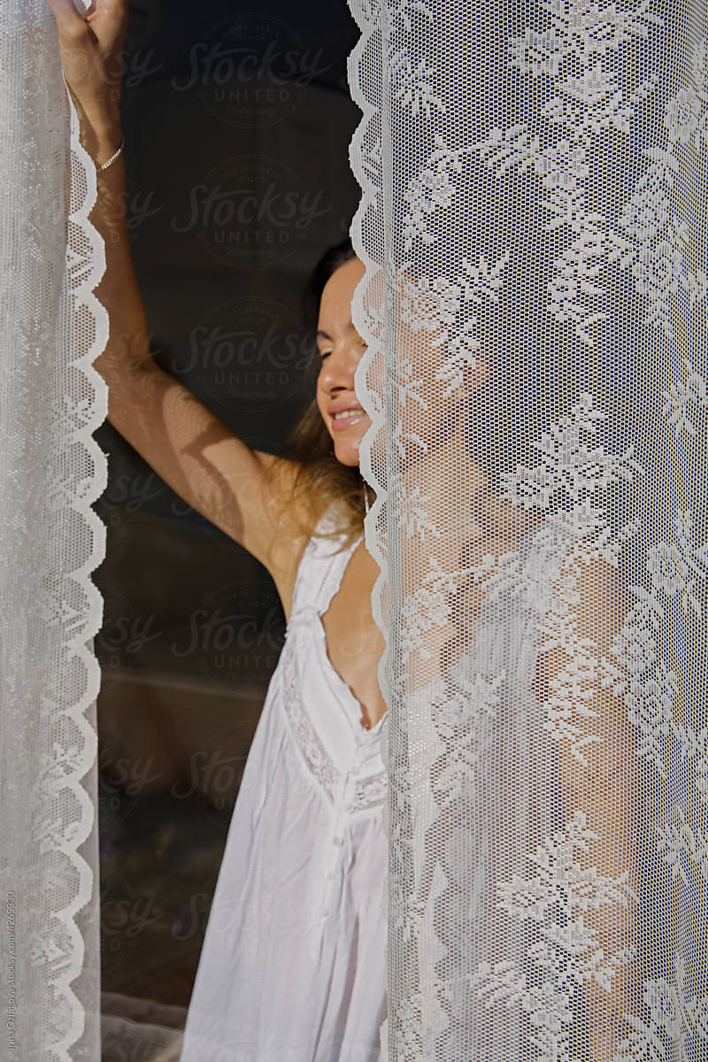Happy woman opening curtains in morning