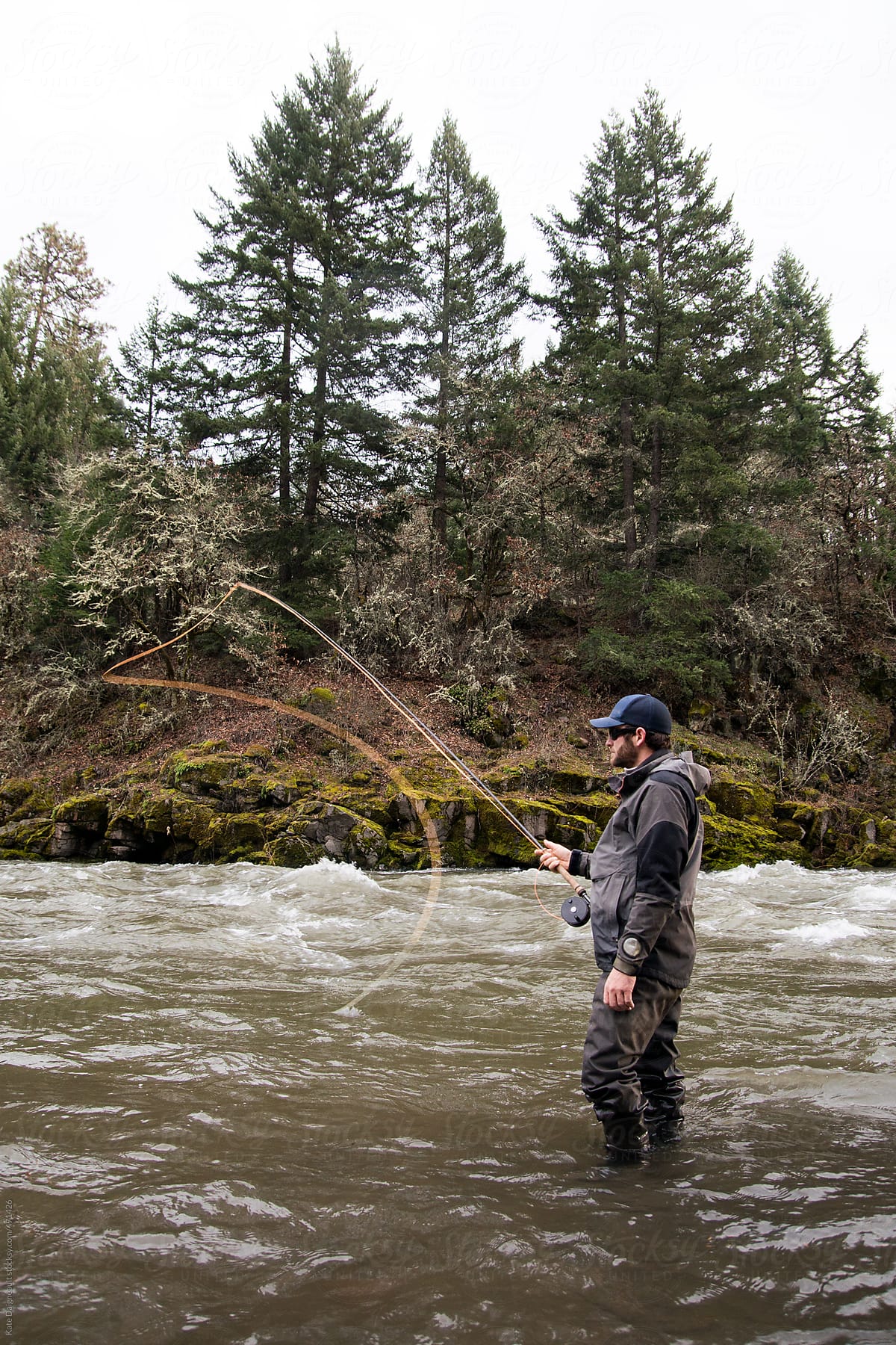 Man stands in the river casting an orange fly fishing line.