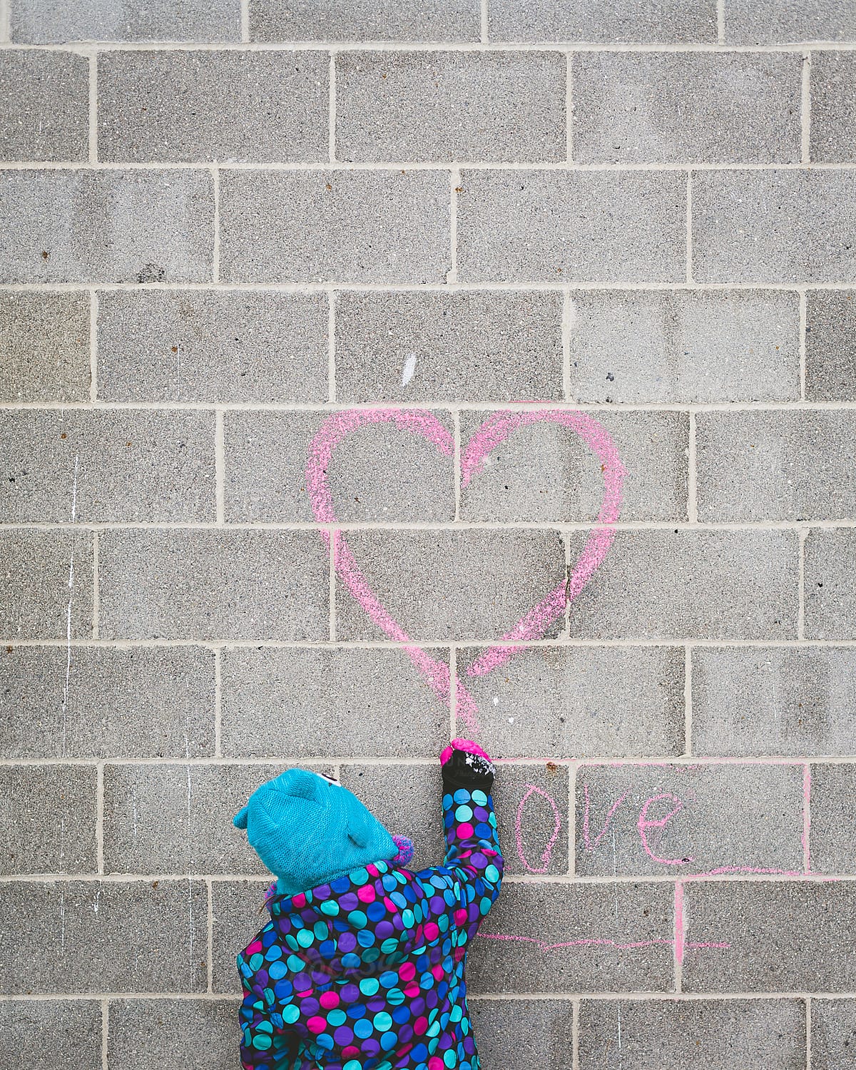 Young girl draws pink heart with chalk on wall above the word \'love\'
