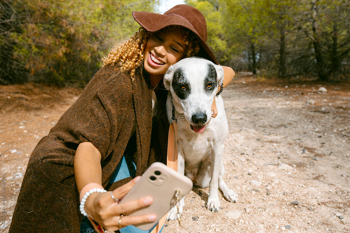 Girl with hat taking a funny selfie with her dog outdoor in sunlight
