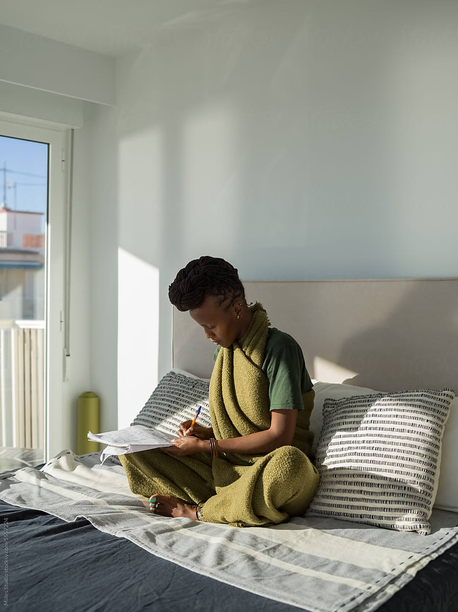 Focused woman doing homework on bed
