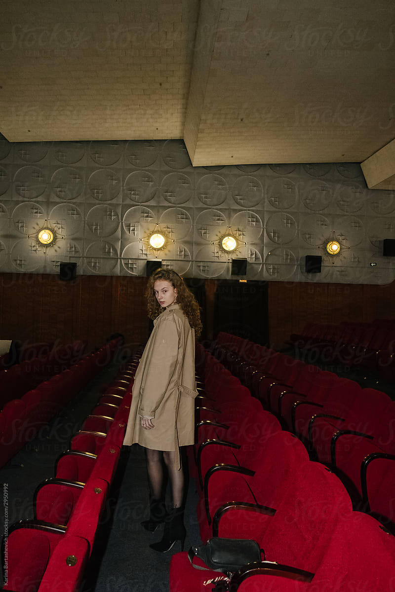 a girl in a cloak with curly hair stands between the rows of red cinema chairs