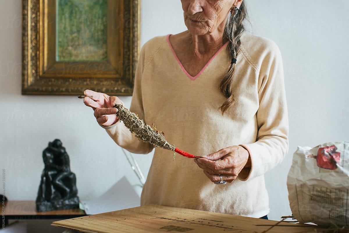 Indoor Portrait of Senior Smoking Woman with Grey Hair Looking at Self-Made Smudge Stick