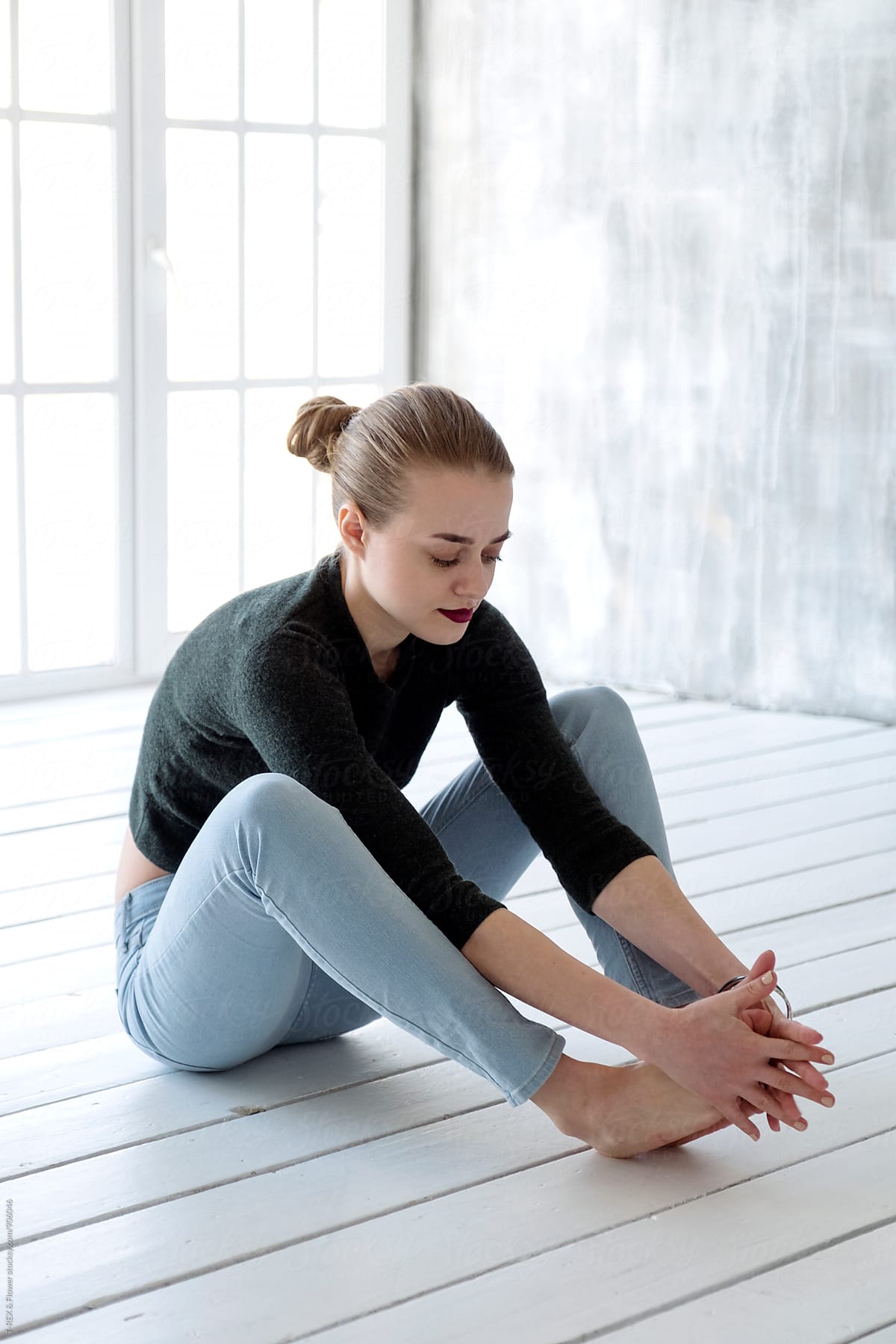 Woman Sitting On Wooden Floor While Touching Her Feet With Hands By Stocksy Contributor Danil