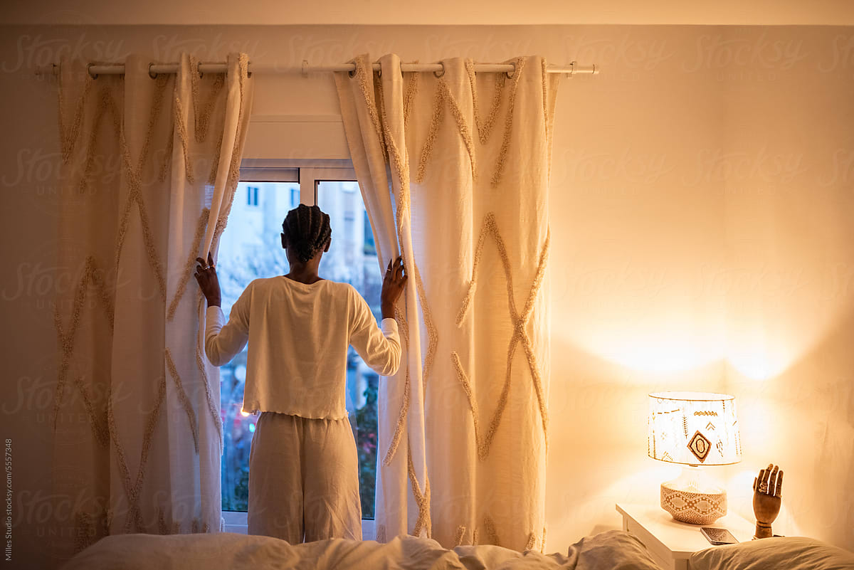 Woman opening curtains in bedroom at home