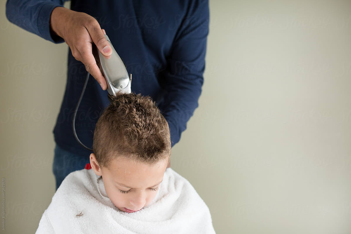 boy ducks head as father clippers back of his head