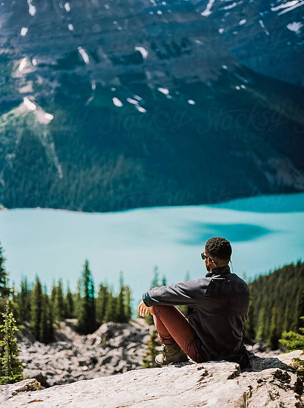 A man sitting high up on a moutain looking down at a lake by Kristen ...