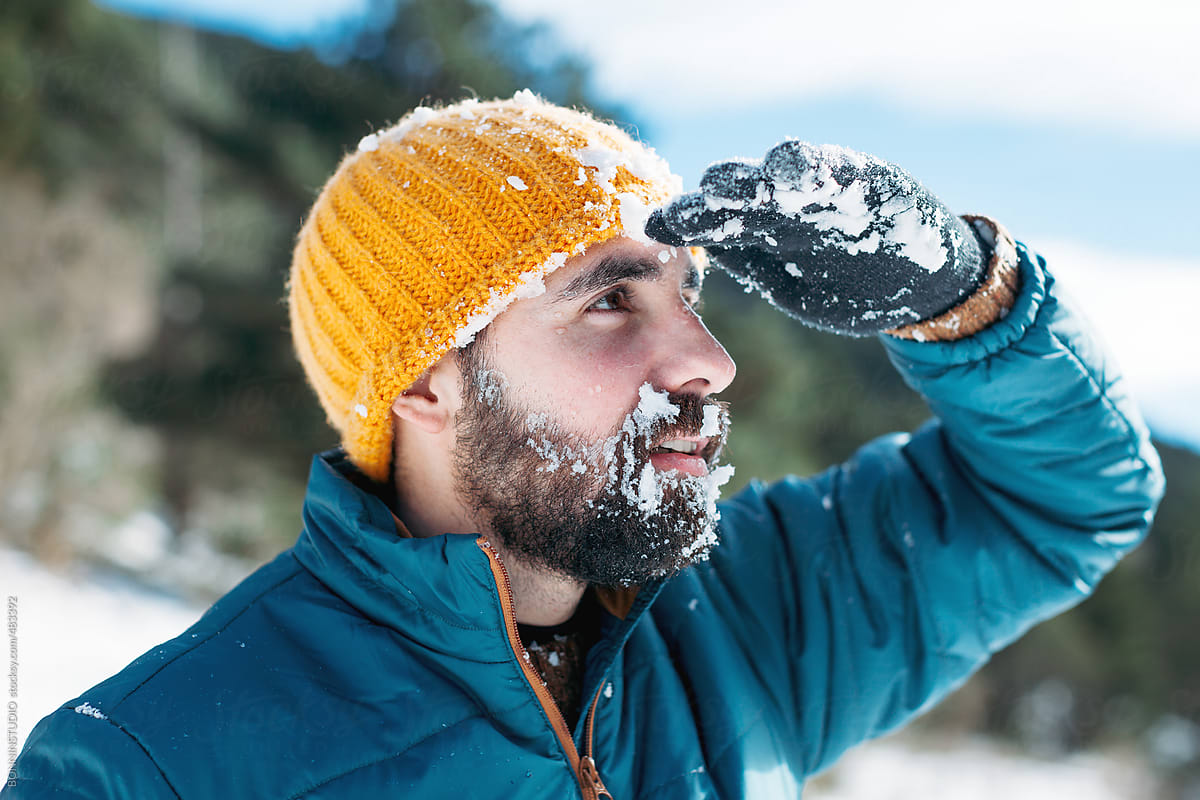 Young bearded man covered with snow looking at a beautiful landscape.