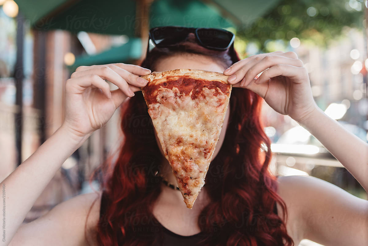 A teenage girl eating pizza in the city