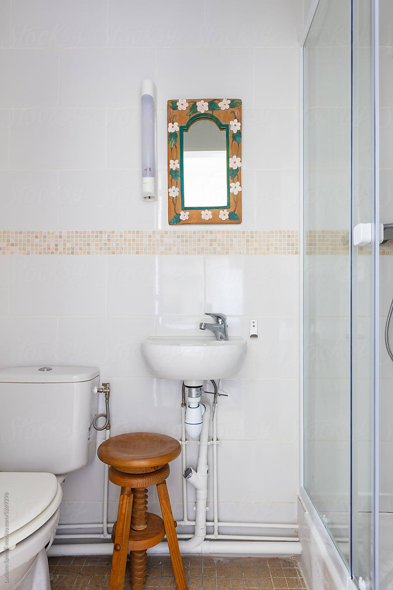 White small toilet with a mirror and a wood stool and glass door