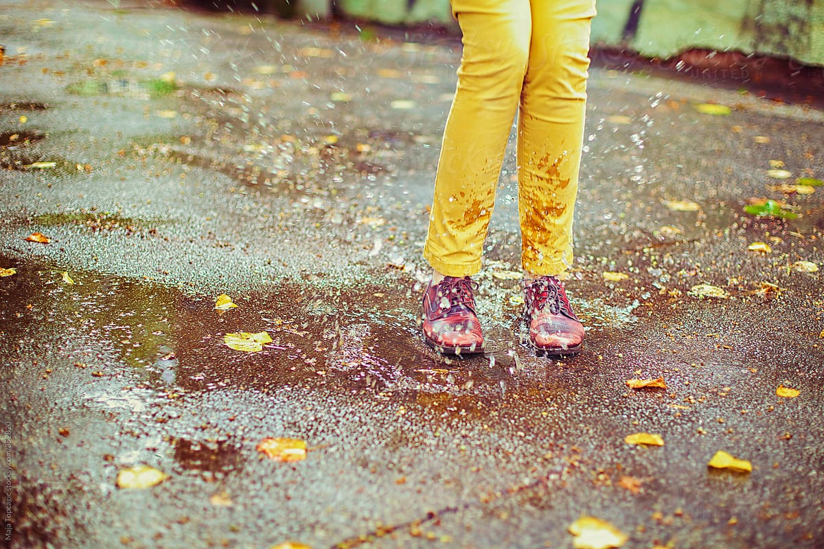 Woman in yellow pants jumping in a puddle of rain