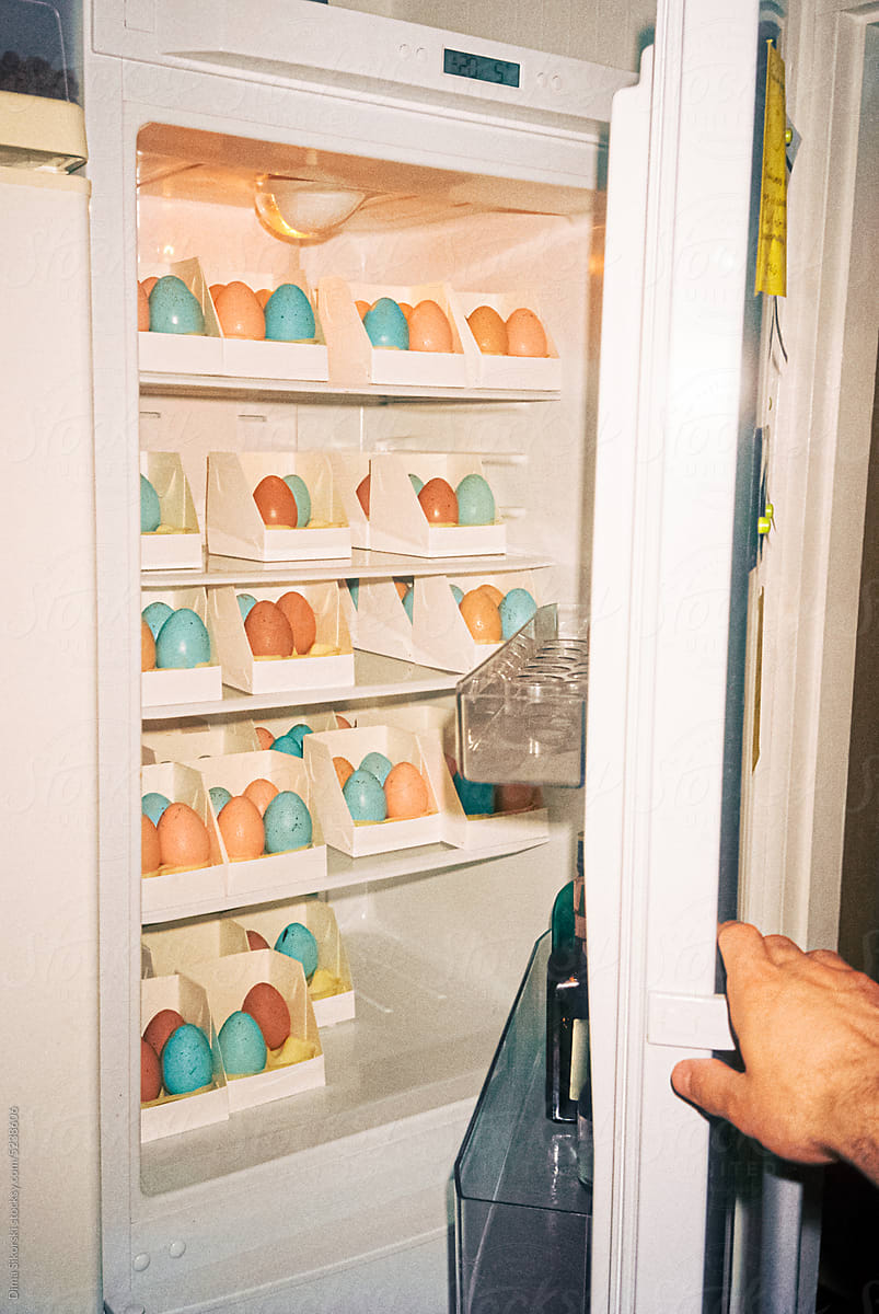 A hand opens a refrigerator filled with lots of Easter eggs