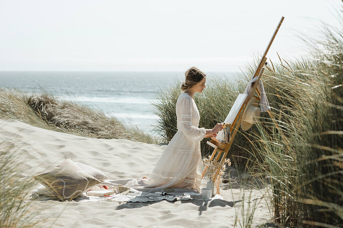 Young woman painting at the coast in the dunes