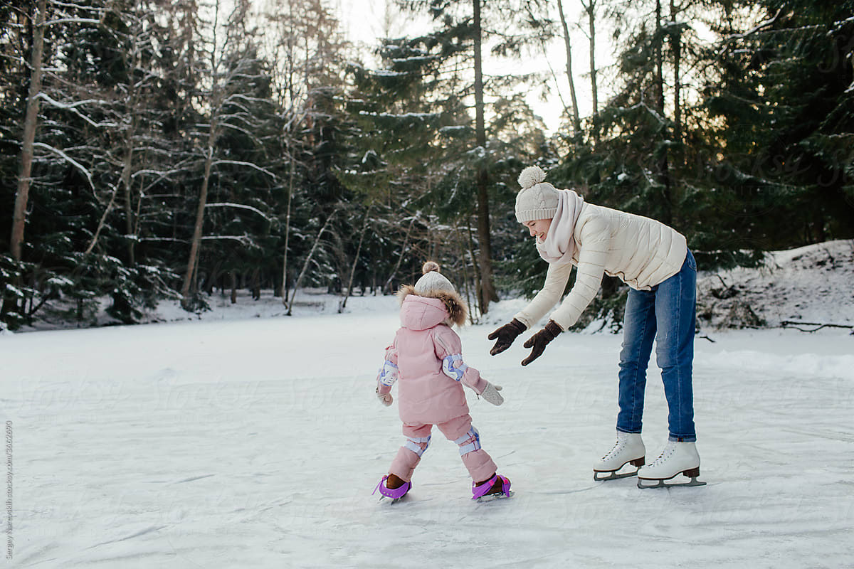 Mother giving support to child learning skating on ice