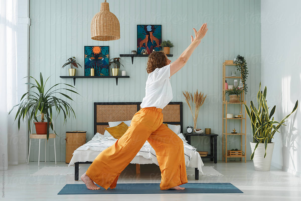 Woman raising arms while doing Warrior pose in bedroom
