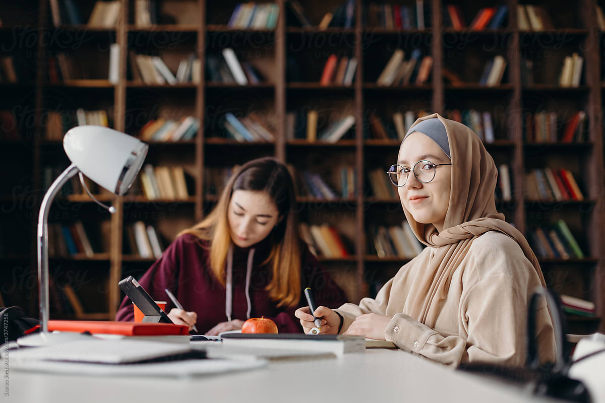 Muslim female student working on project with friend in library