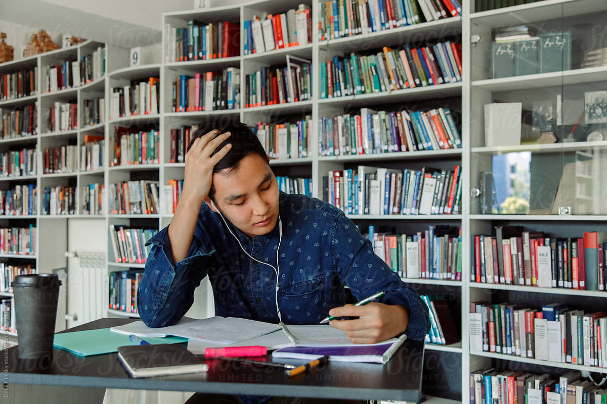 Asian guy listening to music during studies in library