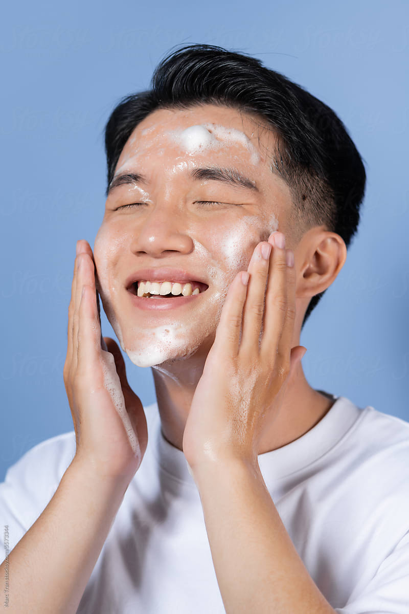 Cheerful young male washing his face using cleansing foam