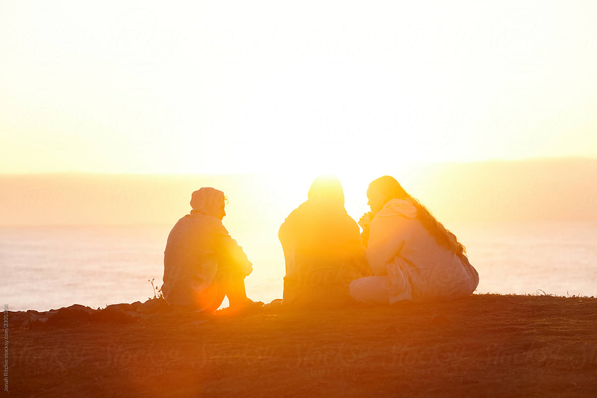A trio of teenage friends sitting together on a headland at sunrise