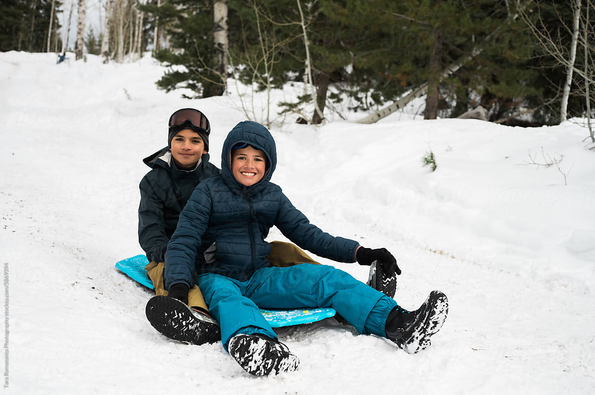 Brothers smiling, seated on a foam sled.