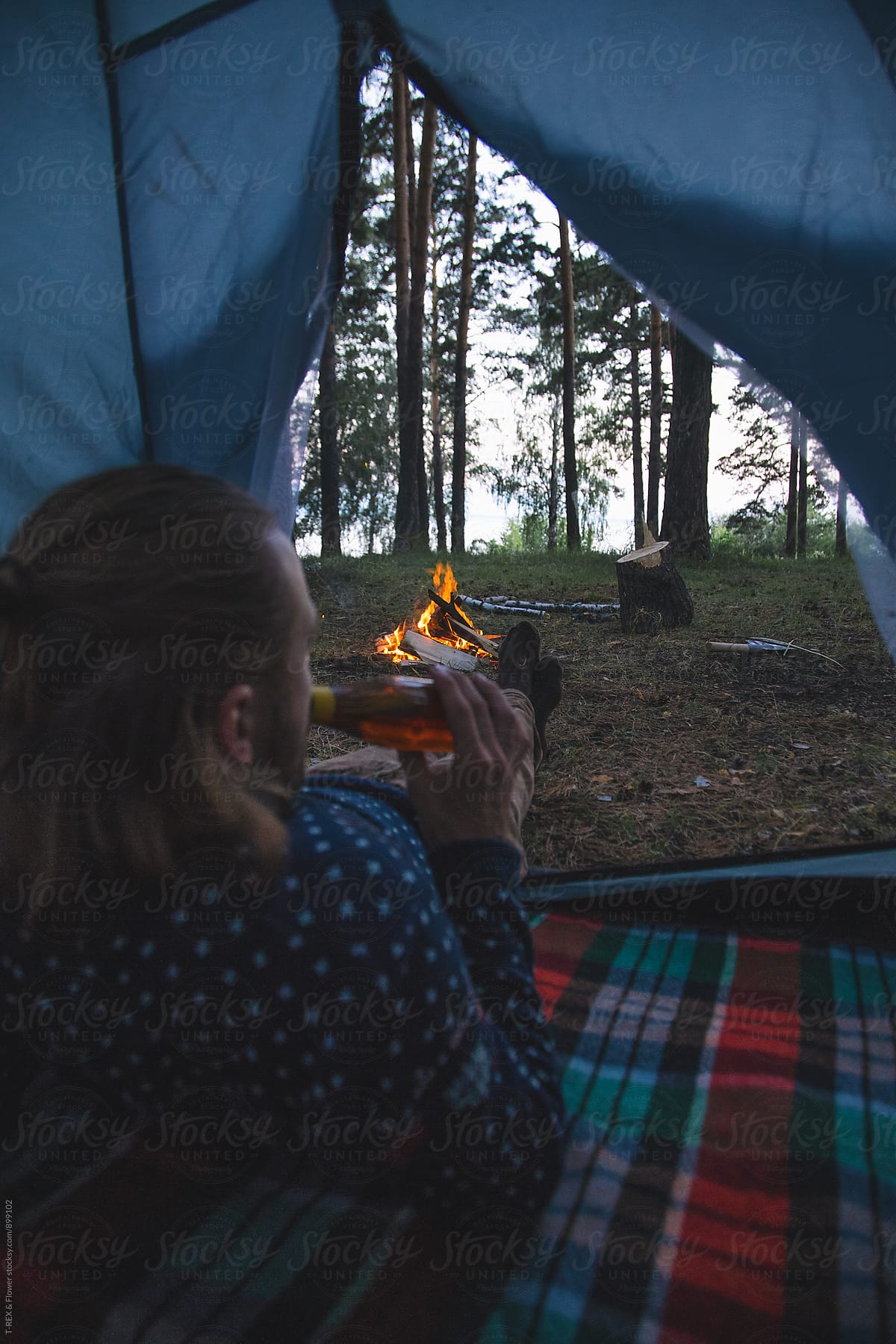 Man in tent drinking beer and looking at campfire