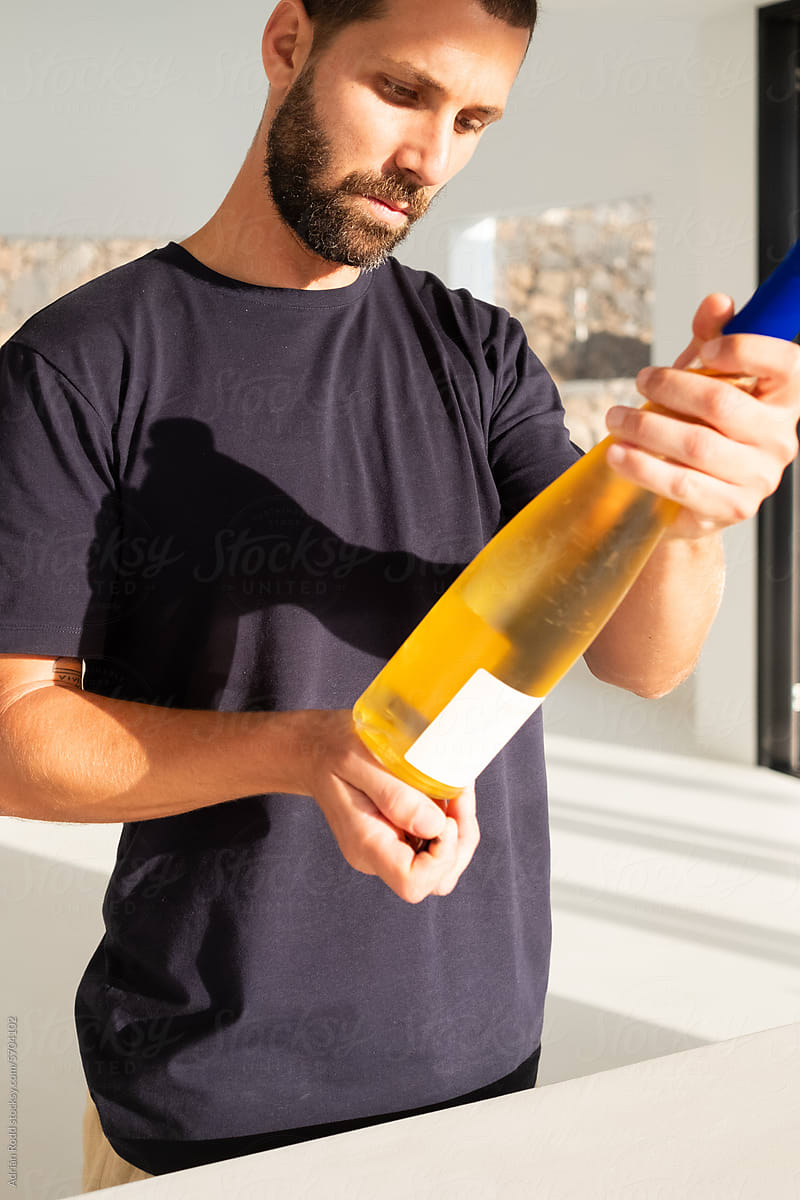 An adult man reads the label of a white wine in the kitchen