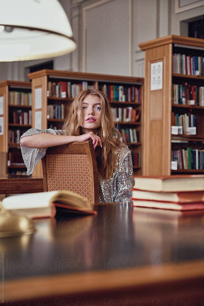 Young beautiful blonde misses a huge library at a table with books