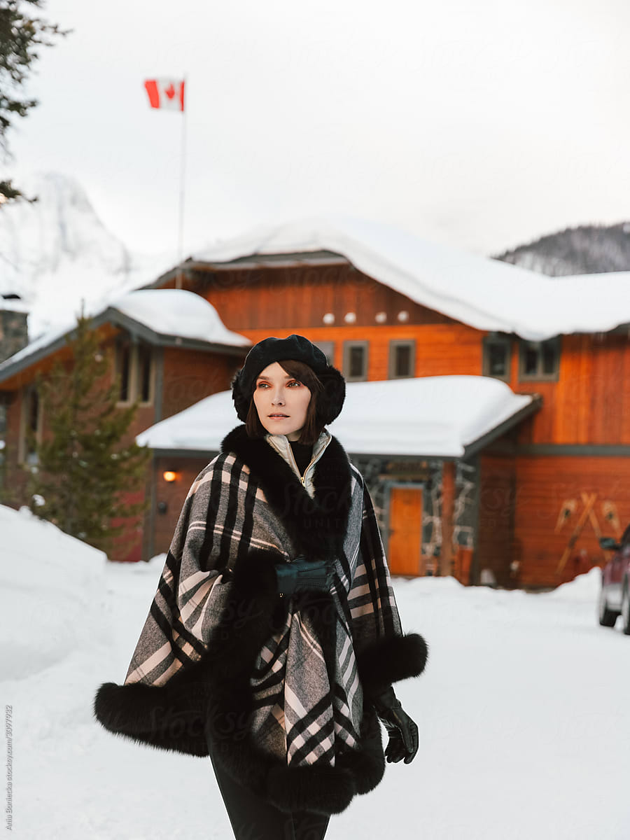 Stylish woman stands in front of lodge in winter.