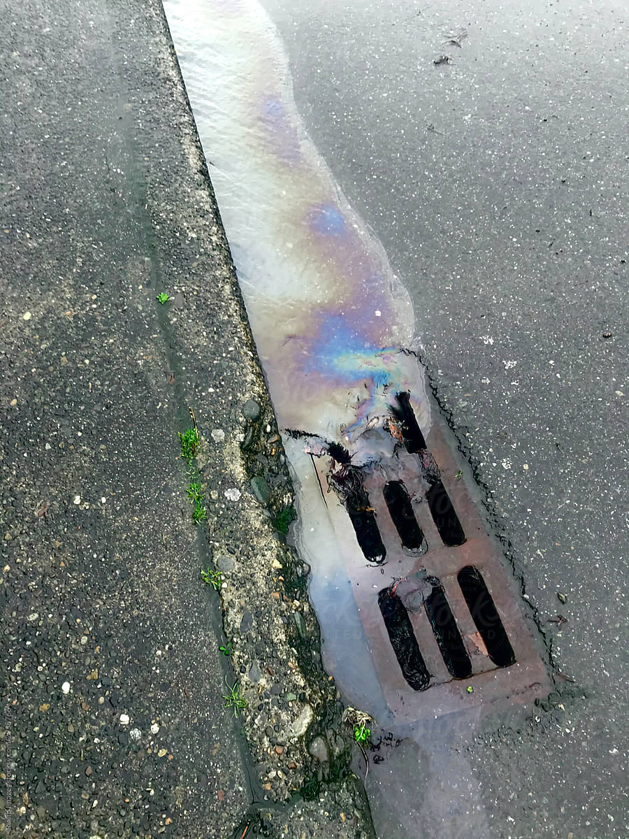 Leaking car oil draining into street sewer during rain storm