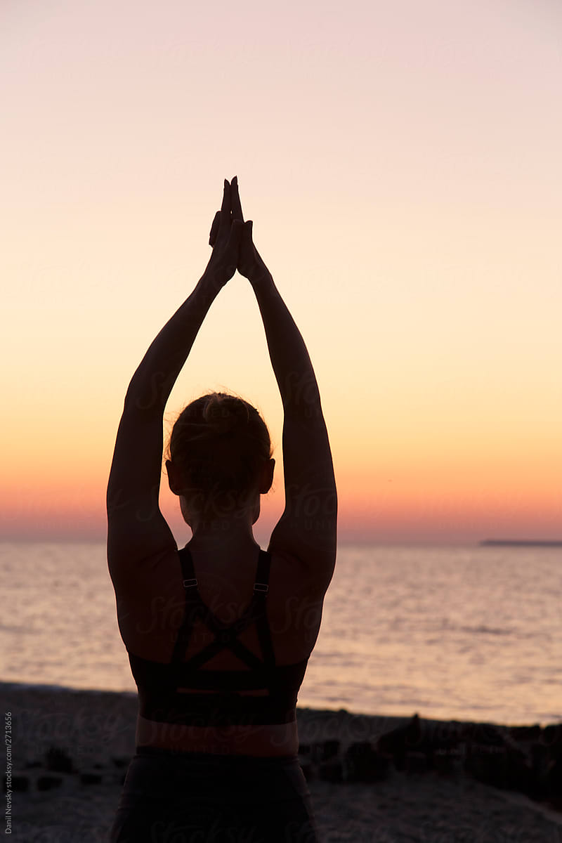 Woman performing yoga posture raising hands at seaside