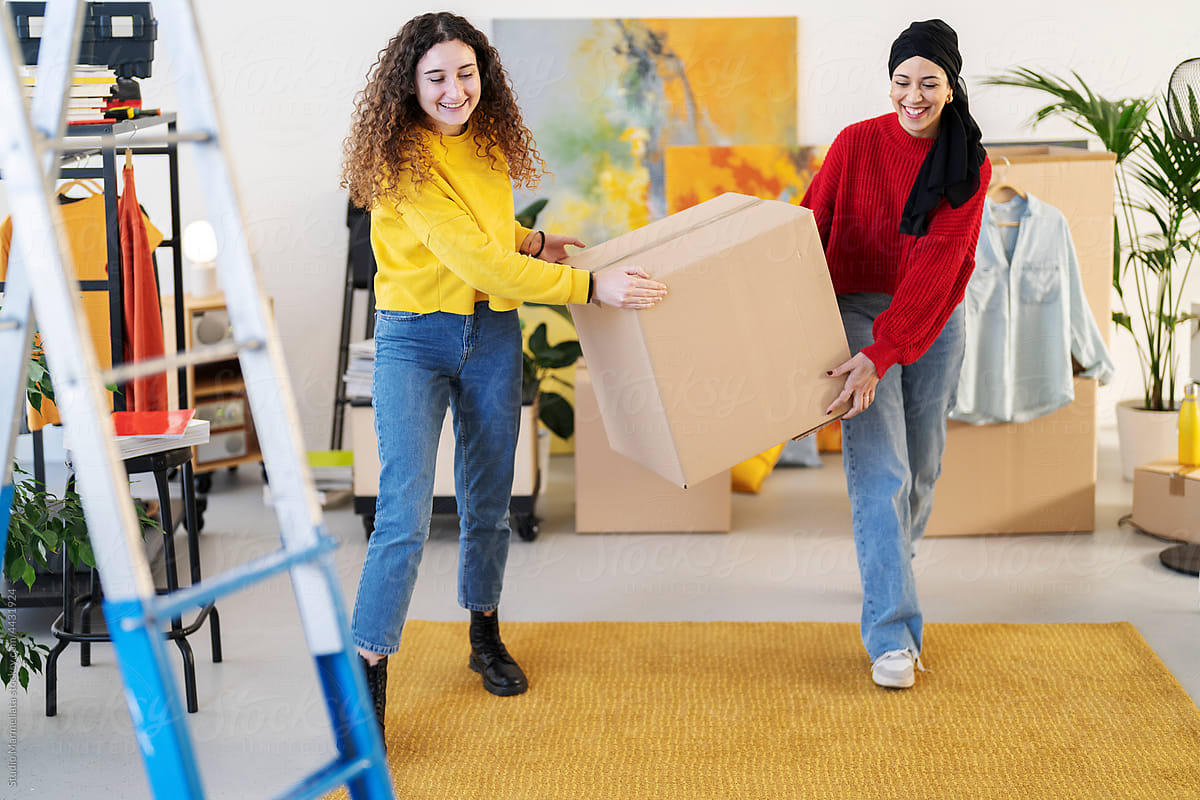 Smiling multiracial women carrying carton box in flat