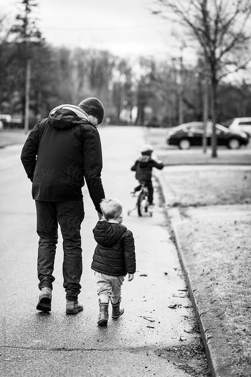 two young boys out for a walk with their father in a suburban neighbourhood.