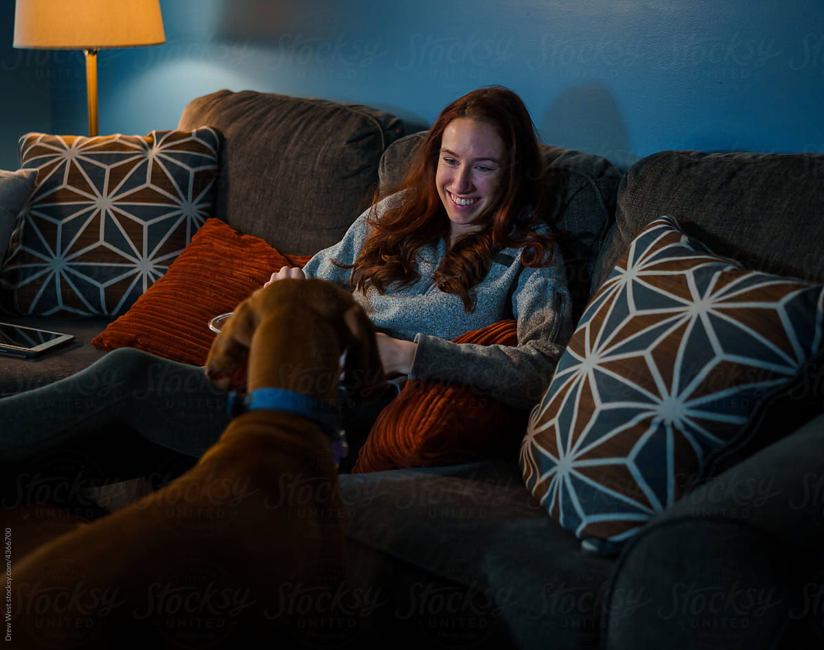 A woman relaxes on the couch with her dog.