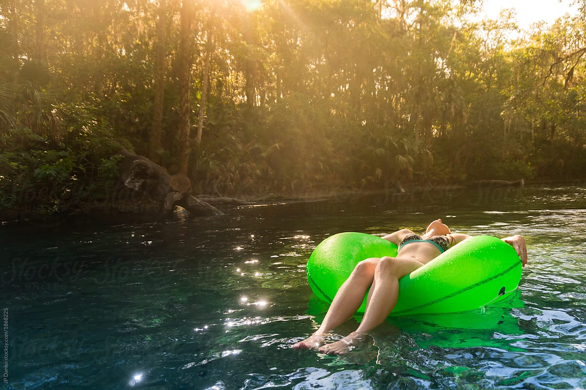 Woman bathed in golden sunlight floats relaxed down lazy Florida freshwater spring river