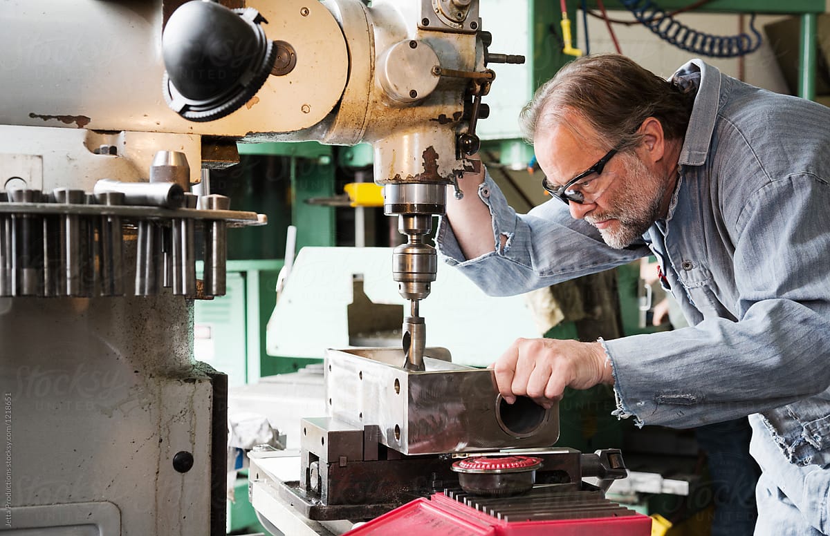 Man in safety glasses using drill press in factory