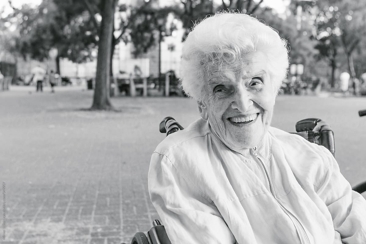 Black-and-white photo of a laughing elderly woman in wheelchair enjoying a sunny day at the park