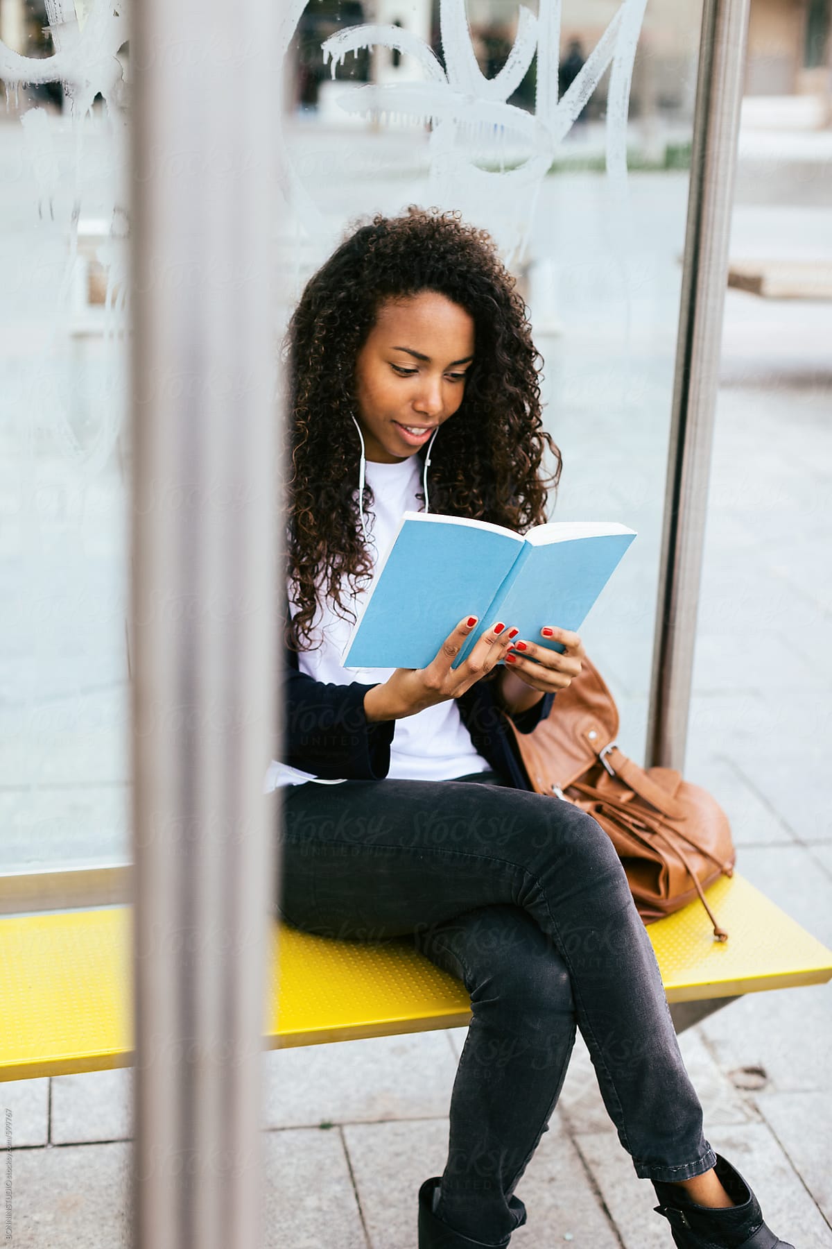 Young african american woman sitting reading a book whilst waiting for the bus.