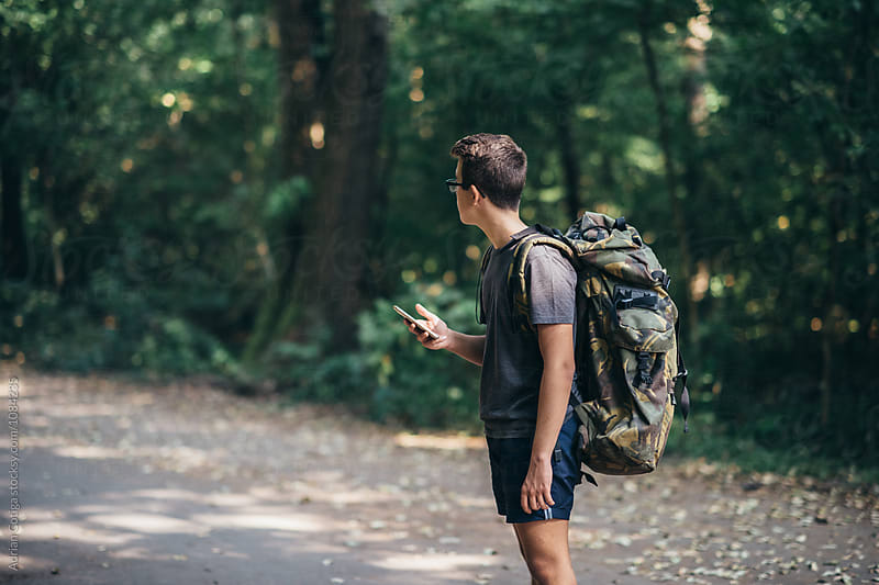 Young teen boy with a backpack exploring the forest, and using smartphone