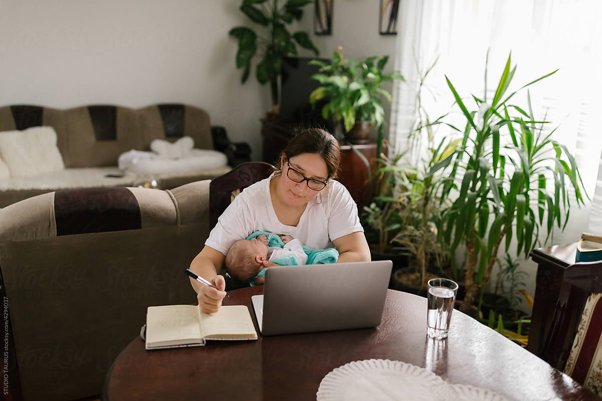 Mother holding baby and working from home via computer
