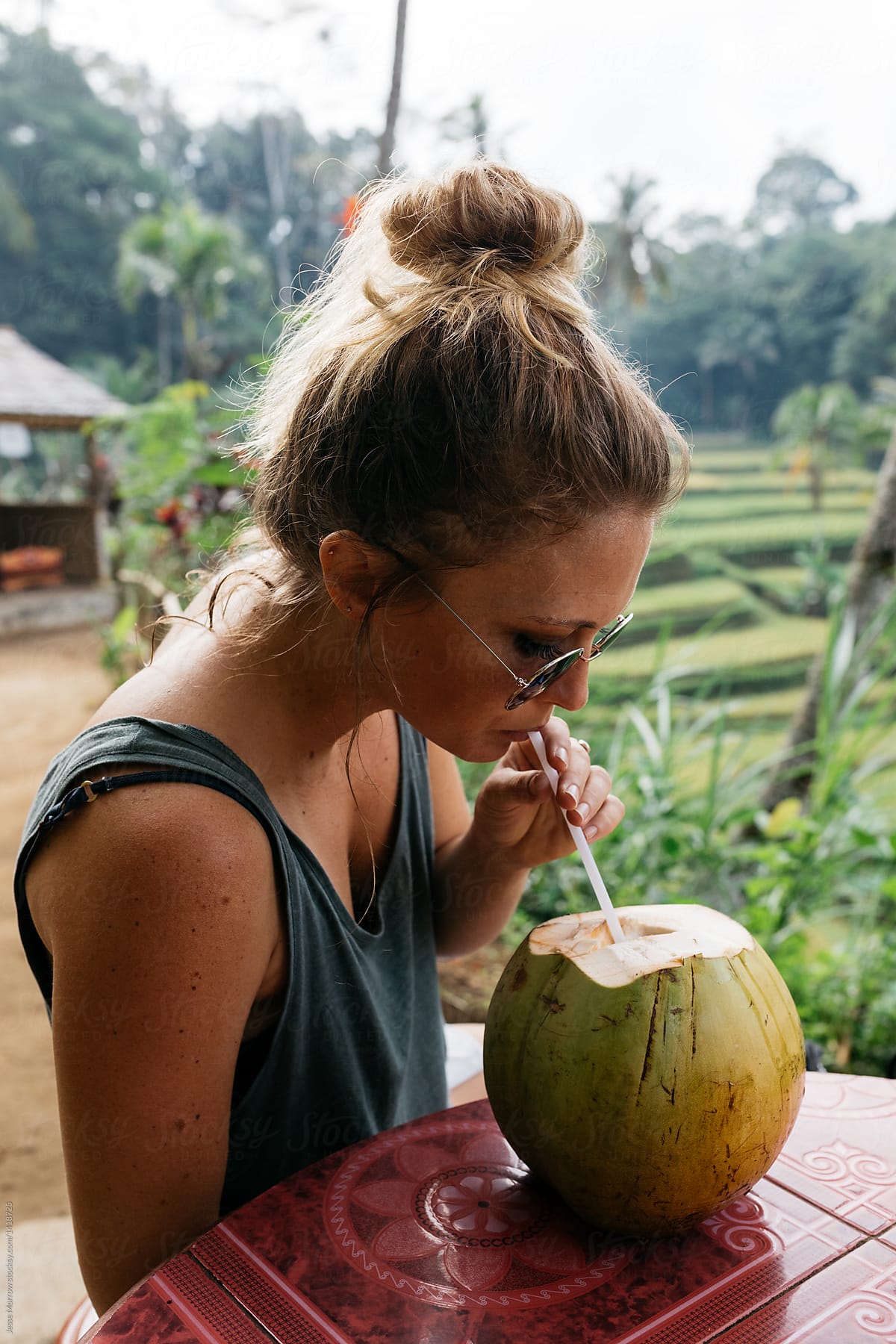 Young woman wearing sunglasses at rice field drinking coconut water from straw