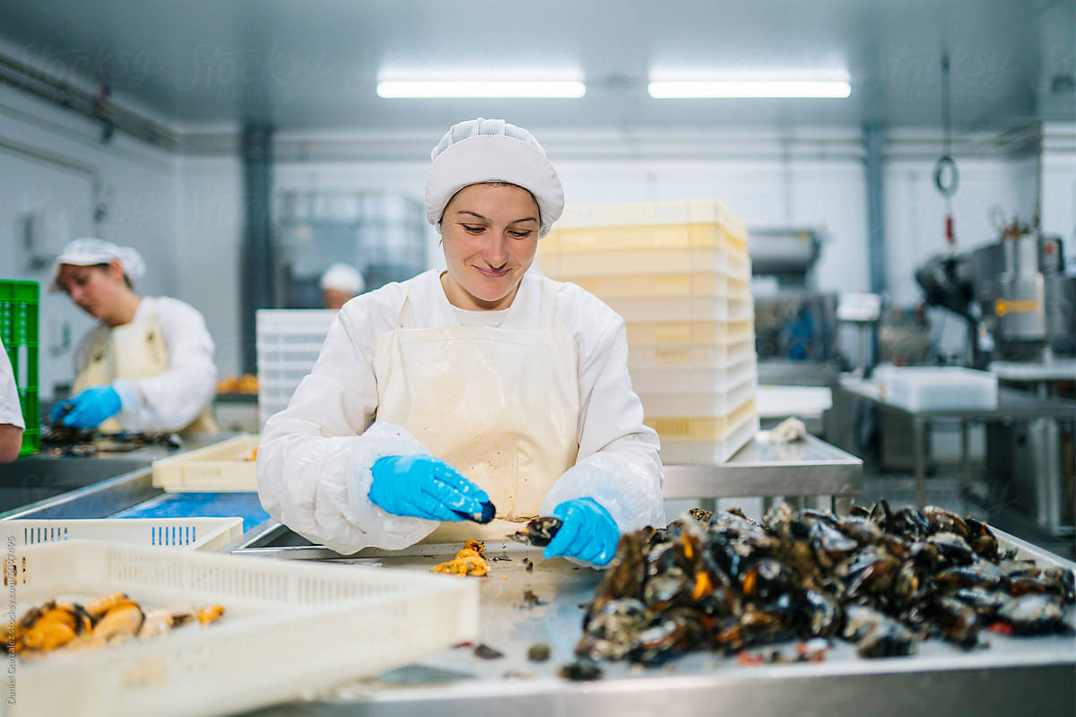 Cheerful female worker peeling mussel in factory