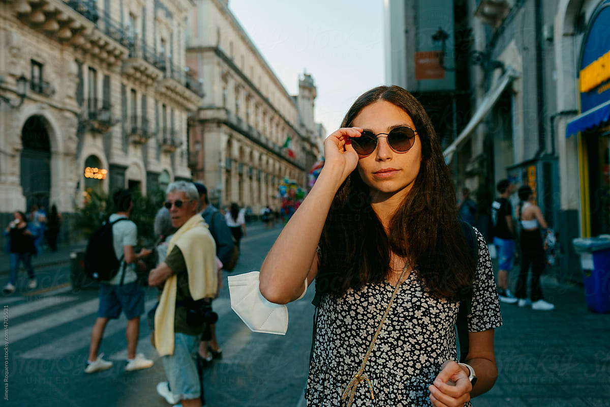 woman with sunglasses in sunlight in city street looking at camera