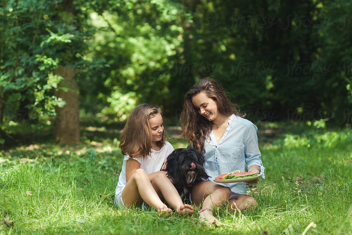 Two girls and their dog getting ready for a picnic with watermelon in the park