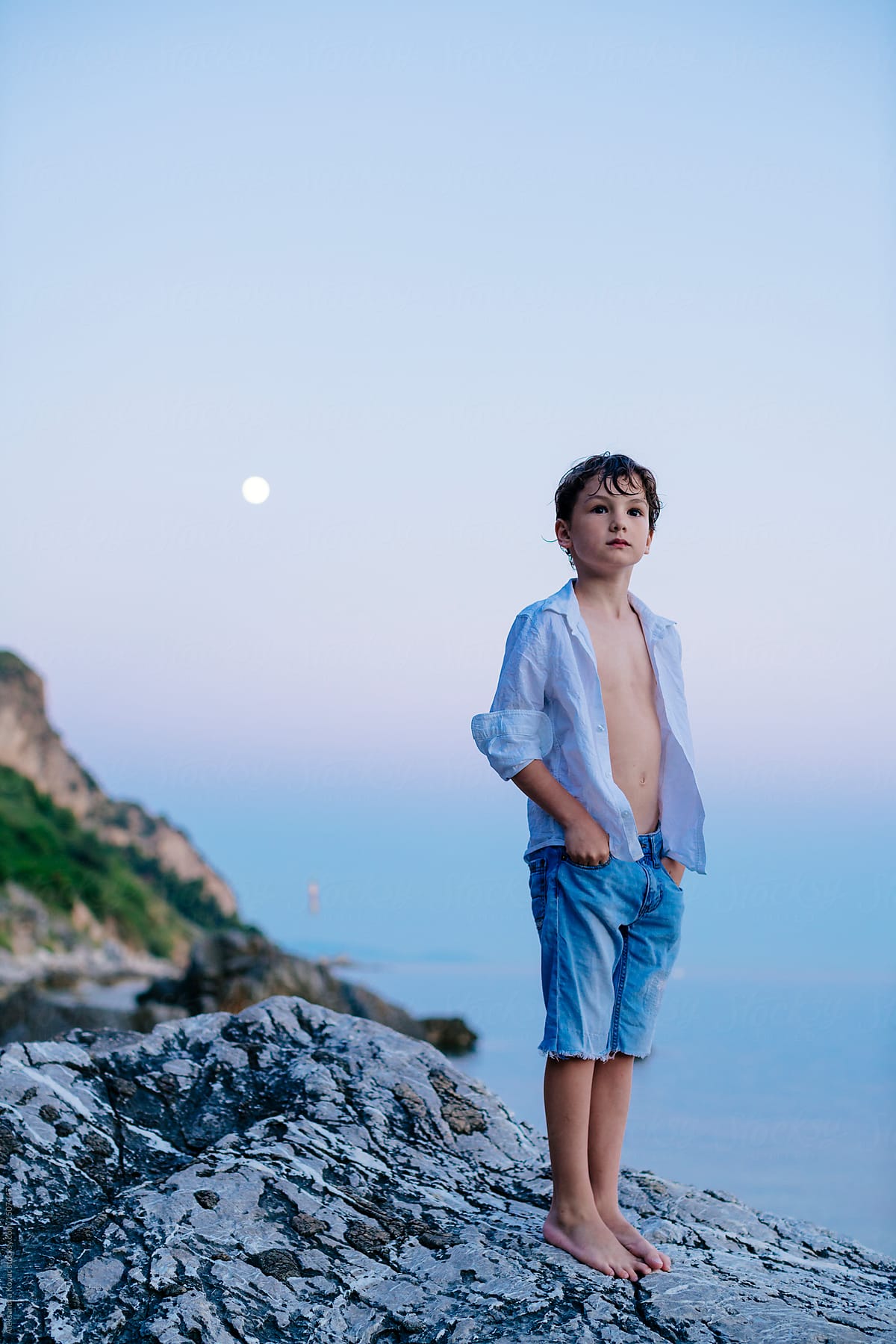 A boy child stands on rock by the sea at moonlight