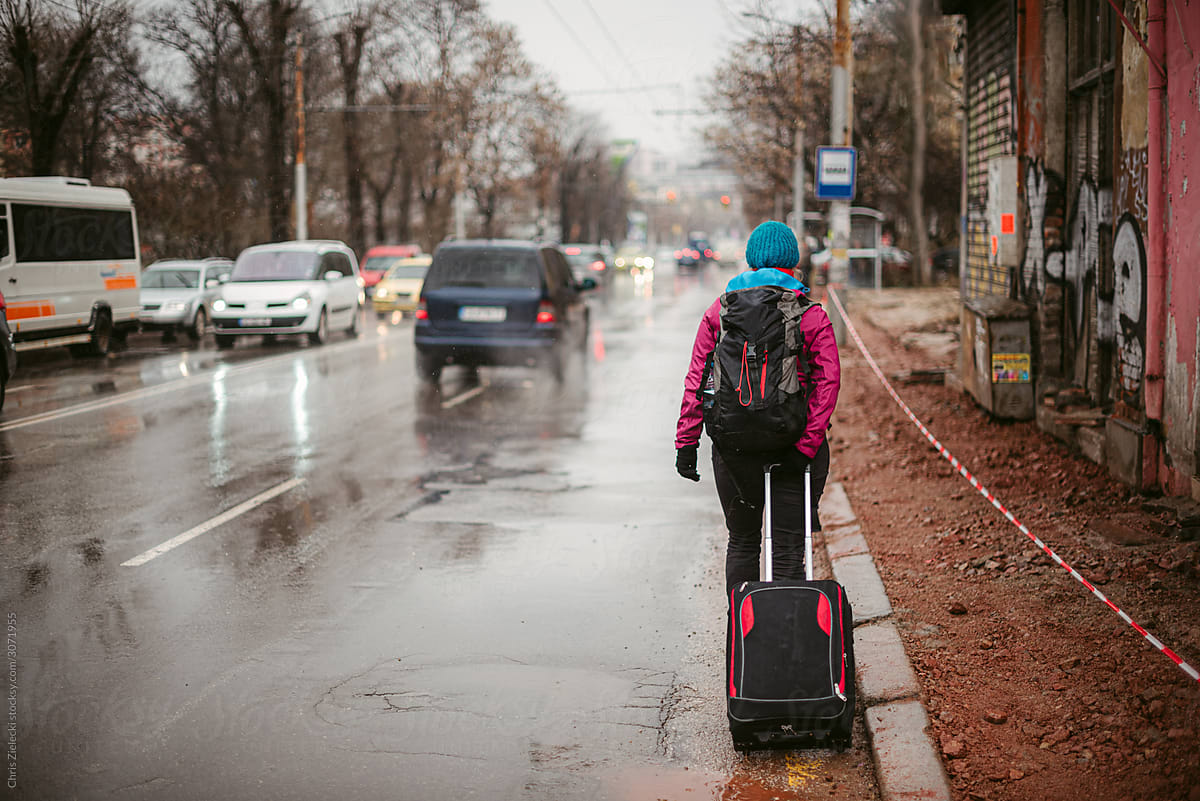 Unrecognizable traveler walking on wet road in city